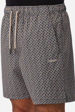 A person wearing Industrie The Savanna Swim Short in navy blue and beige pattern, featuring a white drawstring, quick-dry fabric, and a small embroidered logo on the left thigh.