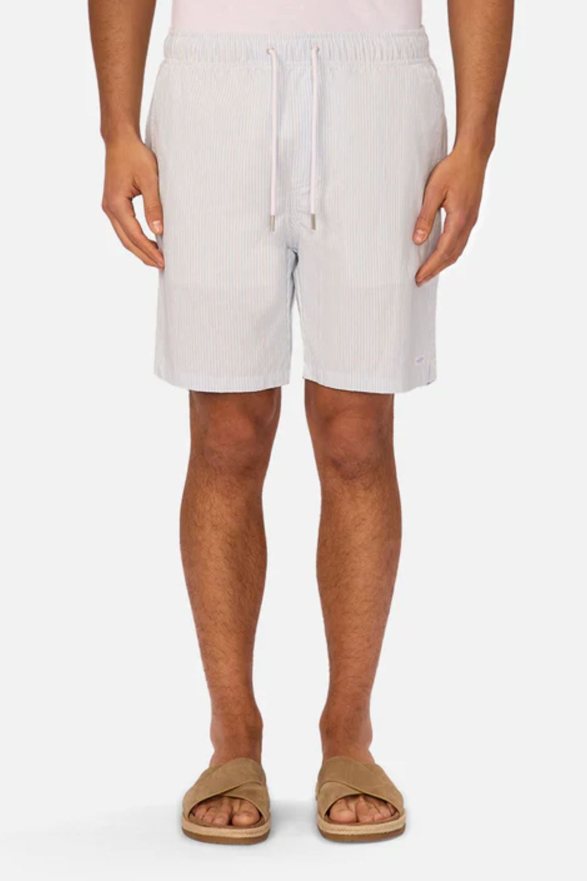The lower half of a person is shown wearing Industrie The Sorrento Short in light pinstripes, paired with a white top and tan slip-on sandals against a plain background.