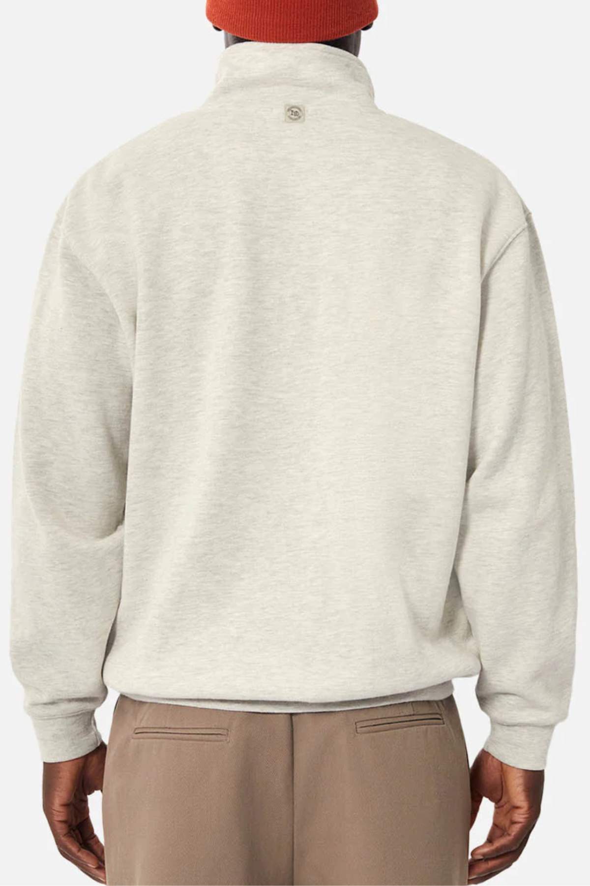 A person is shown from the back wearing the Industrie The Staunton Tracktop in light beige with fleece lining, paired with brown pants and a red beanie, all set against a plain white background.