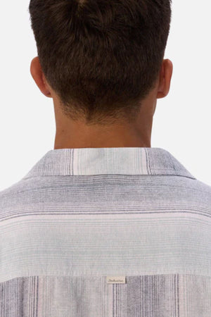 A person with short brown hair is seen from behind, wearing the Industrie The Sunset Short Sleeve Shirt, which features light-colored stripes. The background is plain and light gray.