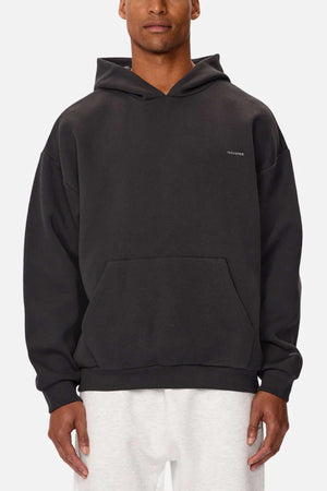 A person wearing a black Industrie The Tech Del Sur Hood with a small chest logo and light-colored pants. Made from advanced athletic fabric, it has a front pocket. A plain white background emphasizes its modern style.