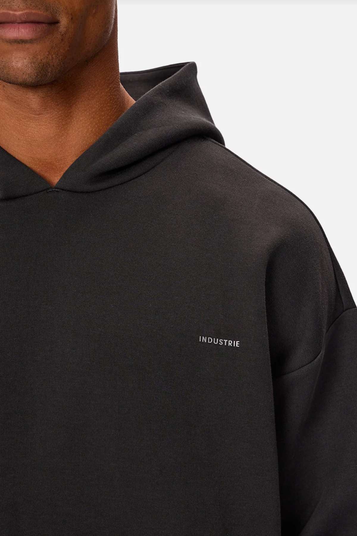 A person wearing the Industrie The Tech Del Sur Hood, featuring "INDUSTRIE" on the chest, exemplifies modernity. Only their lower face and upper body are visible against a plain backdrop, suggesting advanced athletic fabric in its design.