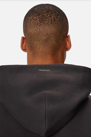 A person wearing the Industrie The Tech Del Sur Hood, featuring "INDUSTRIE" on the back, made from advanced athletic fabrics for a modern yet stylish look, seen from behind against a white background.