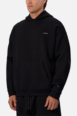 Someone wearing the Industrie The Tech Del Sur Hoodie, a loose-fitting style with a front pocket and subtle white text on the chest and sleeve, stands against a plain light background.