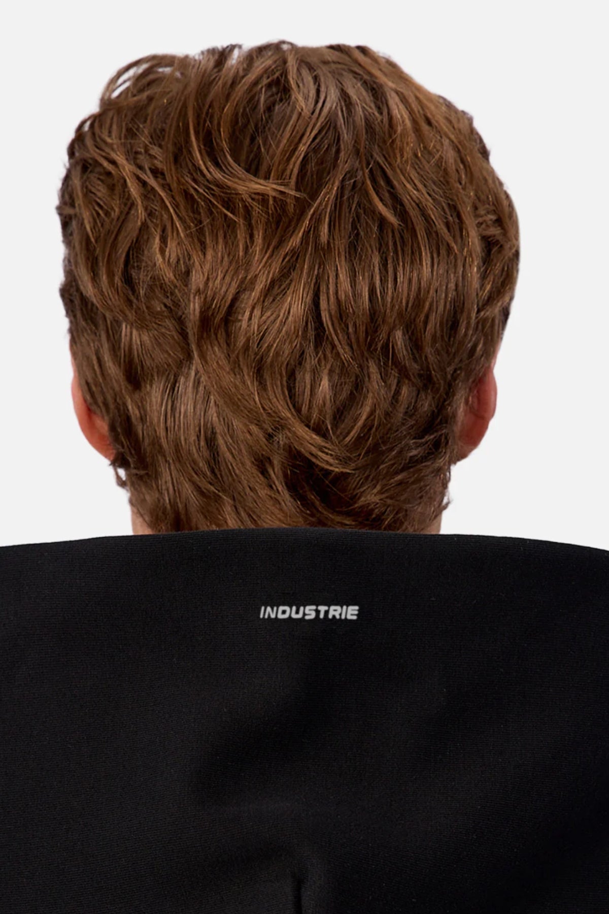 A person with wavy, light brown hair is seen from behind wearing the Industrie The Tech Del Sur Hoodie in black, featuring βINDUSTRIEβ printed in white on the back collar against a plain, light-colored background.