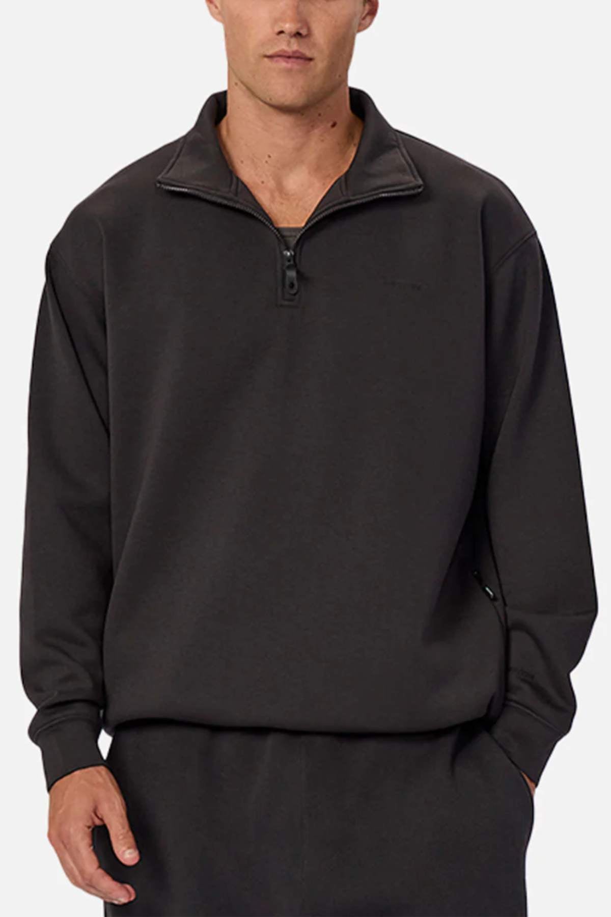A man wears the Industrie The Tech Staunton Track Top, made from athletic fabric with a stand-up collar and matching pants, standing with one hand in his pocket against a plain background.