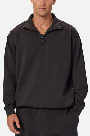 A man wears the Industrie The Tech Staunton Track Top, made from athletic fabric with a stand-up collar and matching pants, standing with one hand in his pocket against a plain background.