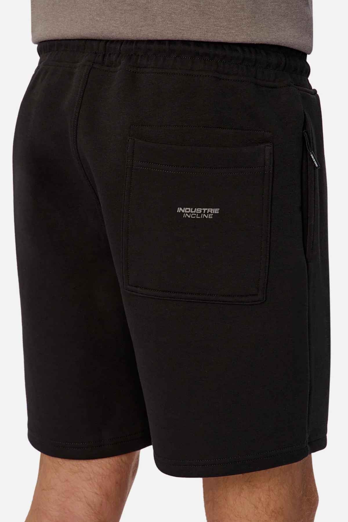 A person wearing black Industrie The Tech Track Shorts with a visible back pocket tag reading "INDUSTRIE INCLINE." Made from athletic material, the shorts feature an elasticated drawstring waist against a plain white background.