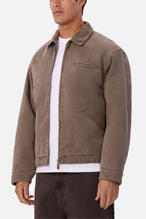 A man wearing the Industrie The Tennesse Jacket in light brown cotton with a collar, styled with a white T-shirt and dark pants, stands against a plain white background.