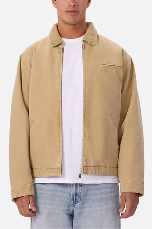 A person wearing the Industrie The Tennesse Jacket, a 100% cotton men's casual jacket in light tan, over a plain white t-shirt and light blue jeans, standing against a plain white background.