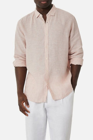 A person wearing the Industrie The Tennyson Linen Blend Shirt in light pink, styled with rolled-up sleeves, pairs it with white pants and stands against a plain white background.