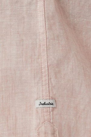 Close-up of a light pink fabric with a visible seam and a small label reading "Industrie," taken from the Industrie The Tennyson Linen Blend Shirt. The fabric has a textured appearance, showcasing its versatility, and the lightweight label is sewn into the seam.