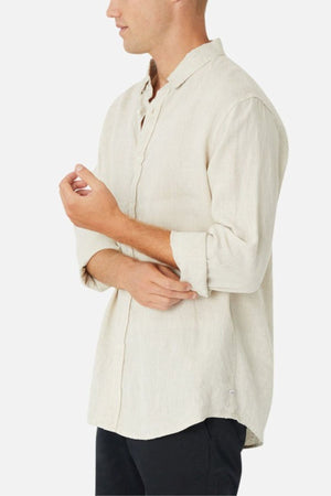 Wearing the Industrie The Tennyson Linen Blend Shirt in a light hue, with its spread collar and rolled-up sleeves, someone pairs it stylishly with black pants. They stand against a plain white background, slightly turned to the side, adjusting their sleeve—a perfect look for summertime.
