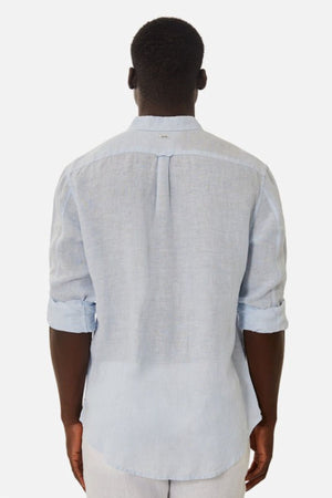 A person is showcasing the effortless elegance of the Industrie The Tennyson Linen Blend Shirt, a versatile light blue garment with rolled-up sleeves. Featuring a back pleat, this lightweight shirt provides both comfort and style as they face away from the camera against a plain white background.