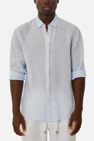 A person wearing the Industrie The Tennyson Linen Blend Shirt in light blue, with the sleeves casually rolled up. The shirt is buttoned up and paired with versatile light-colored pants against a plain white background.