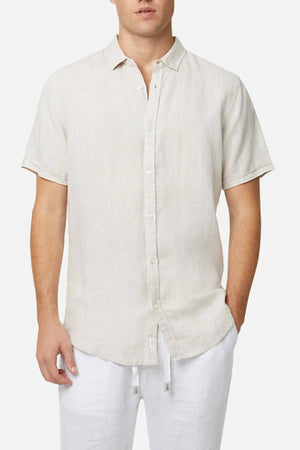 A man wears the Industrie The Tennyson Linen Short Sleeve Shirt and white pants, hands in pockets, standing against a plain white background—perfect for breathability and relaxed style.