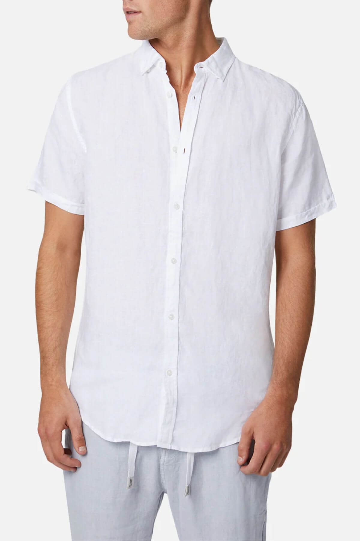 A man in the Industrie Tennyson Linen Short Sleeve Shirt exudes casual style with its collared design. He pairs it effortlessly with light, loose-fitting linen pants against a plain white background.