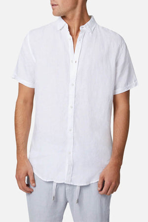 A man in the Industrie Tennyson Linen Short Sleeve Shirt exudes casual style with its collared design. He pairs it effortlessly with light, loose-fitting linen pants against a plain white background.