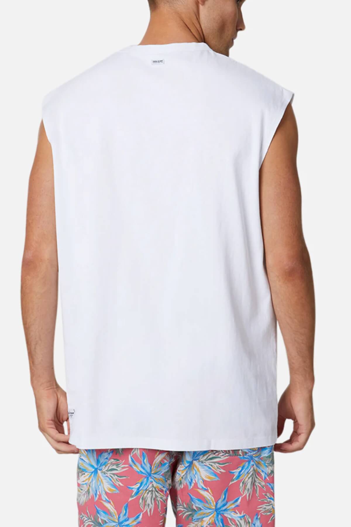 A man wears the Industrie The Triple G Sleeveless Tee paired with floral shorts featuring pink and blue patterns, showcasing their 100% cotton fabric amidst a plain white background, emphasizing the relaxed fit of his attire.