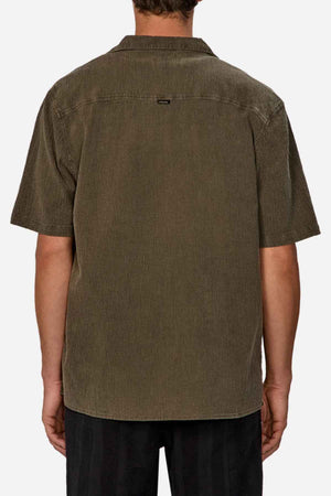A person in the Industrie The Washed Magna Short Sleeve Shirt, with its olive green color and oversized fit, stands with their back to the camera. Made from breathable fabric and featuring a small label near the collar, it pairs well with dark pants against a plain white background.