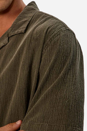 Close-up of a person wearing the Industrie The Washed Magna Short Sleeve Shirt in olive-green. The image focuses on the left shoulder and part of the chest, showcasing the distinctive crinkled pattern and breathable fabric. The oversized fit contributes to a laid-back style against a plain white background.