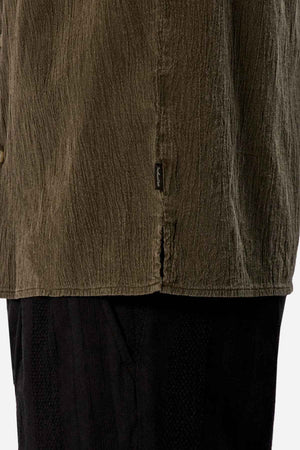 Close-up of a person wearing the Industrie The Washed Magna Short Sleeve Shirt in textured olive green, featuring an oversized fit and a small side label, paired with black pants. The attention is on the breathable fabric and the detail of the shirt's hem.
