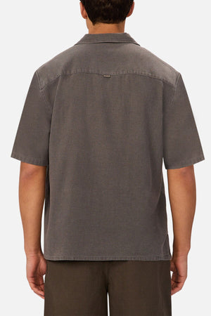 A man is shown from behind wearing the Industrie The Washed Menorca Short Sleeve Shirt in gray and dark brown shorts against a plain white background.