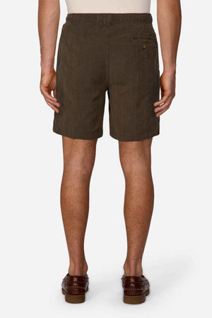 A person dressed in Industrie The Washed Salamanca Short and brown loafers is seen from behind. The textured cotton blend shorts showcase a tailored fit with a side pocket button, contrasting against a plain white background.