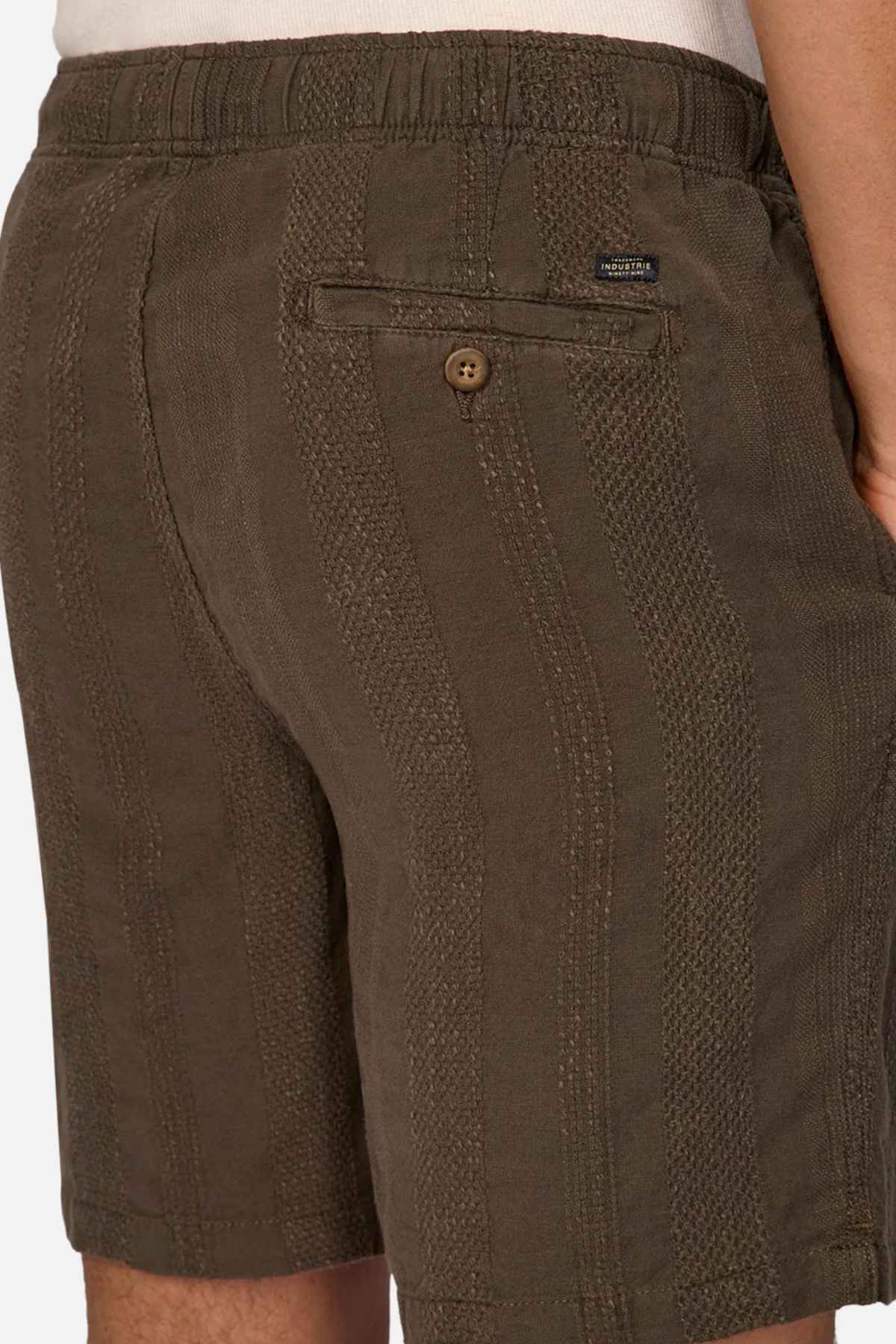 A person wearing green Industrie The Washed Salamanca Short, made from a textured cotton blend with an elastic waistband and a single back pocket, stands against a plain background.