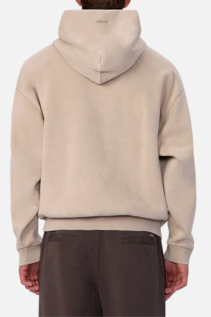 A person wears the Industrie The Washed Tech Hood in beige with the hood up, styled with dark brown pants against a plain light background—ideal for casual everyday looks.
