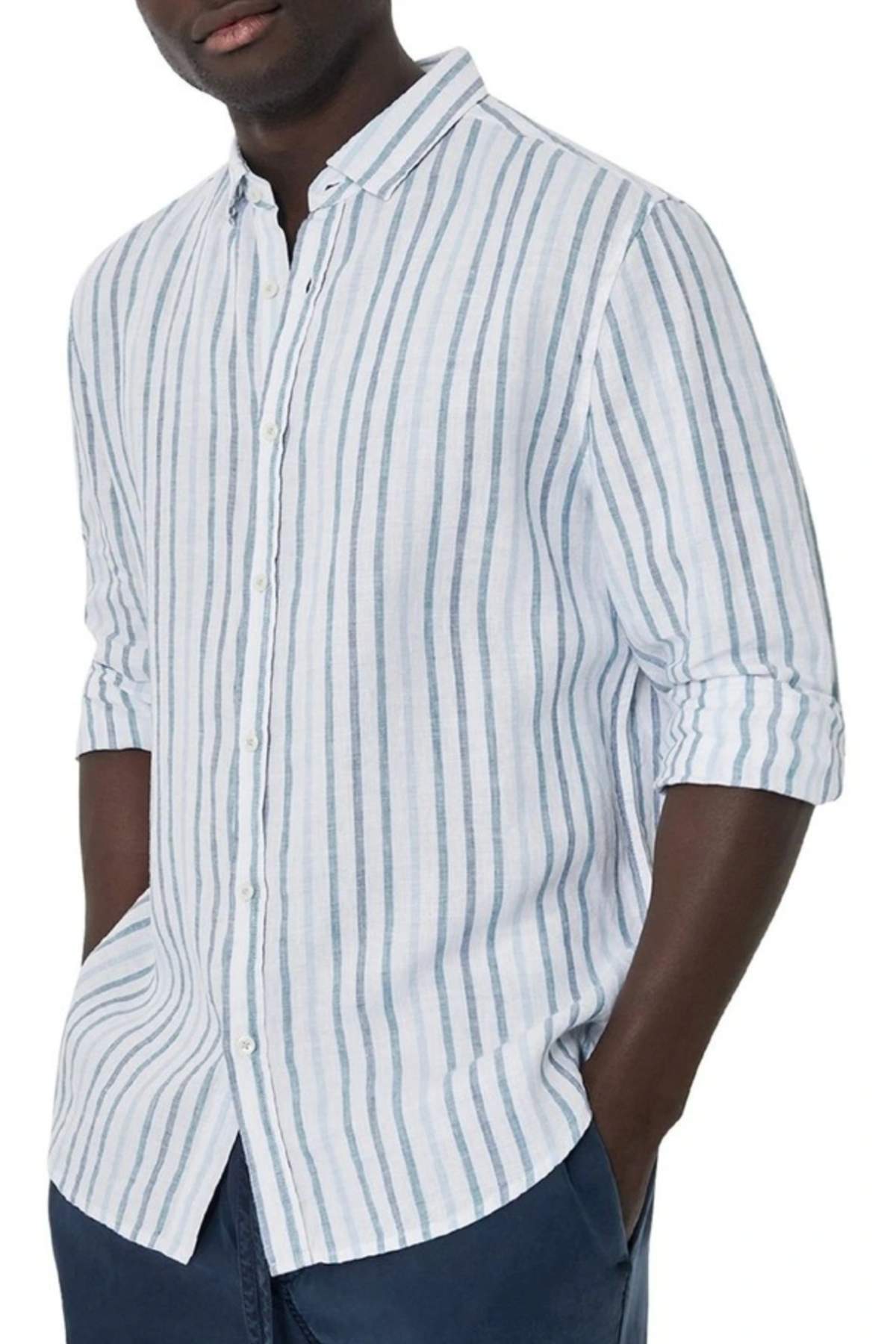 A person wears the Industrie The Webster Long Sleeve Shirt, featuring a relaxed fit with light blue and white stripes. They have rolled-up sleeves, navy pants, and their hands in their pockets against a plain white background.