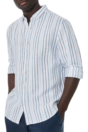 A person wears the Industrie The Webster Long Sleeve Shirt, featuring a relaxed fit with light blue and white stripes. They have rolled-up sleeves, navy pants, and their hands in their pockets against a plain white background.