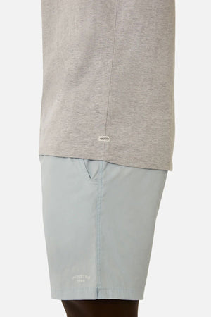 A person wearing a light gray Industrie The Triple G Sleeveless Tee, showcasing a relaxed fit and a small label near the hem, paired with light blue shorts with side pockets, stands against a plain background.