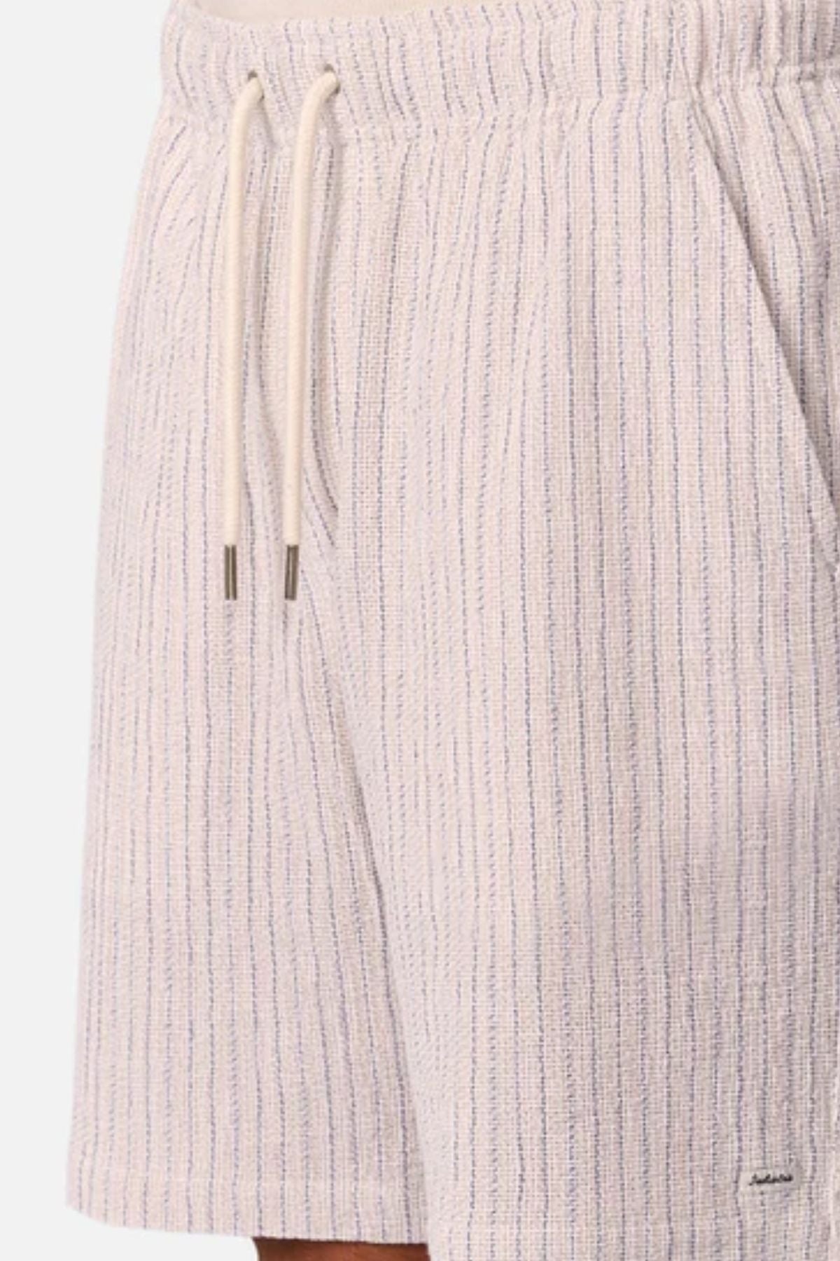 Close-up of a person wearing Industrie The Frescati Short in light-colored, textured linen with thin vertical stripes, metal-tipped drawstrings, and a small rectangular hem tag—ideal men's summer shorts for warm days.