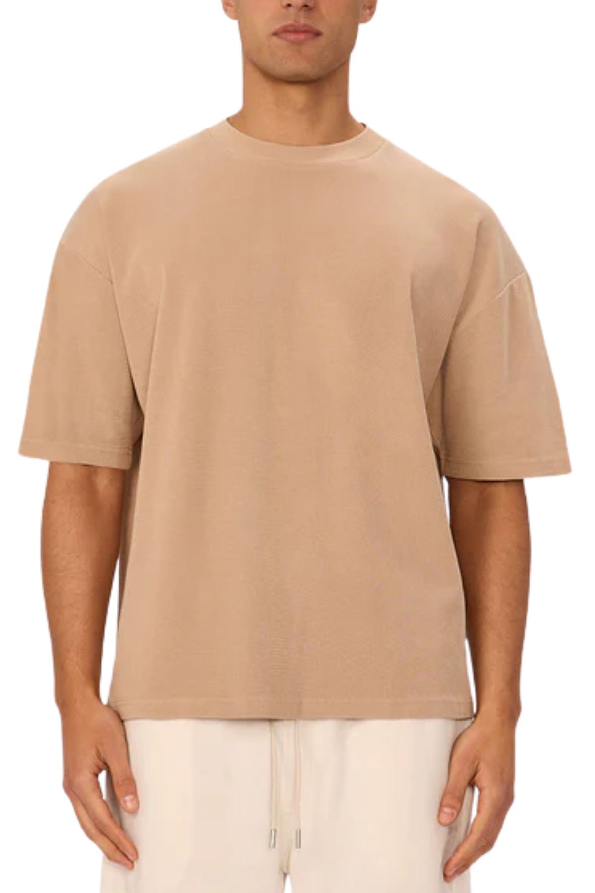 Someone wearing the Industrie The Marlon Tee, a loose-fitting, short-sleeve beige relaxed fit shirt, paired with light drawstring pants, stands facing forward against a plain white background.