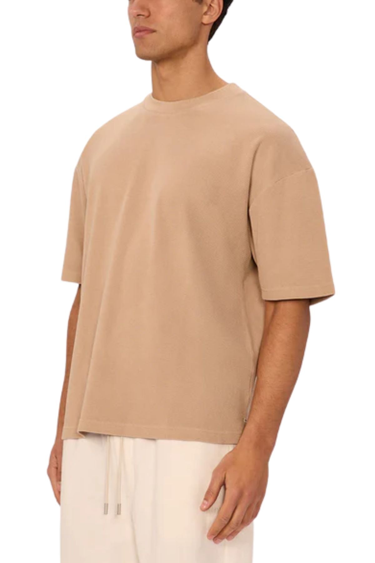 A person wears the Industrie The Marlon Tee in beige, featuring a relaxed fit and waffle knit fabric, paired with light drawstring pants. They stand against a plain white background, emphasizing the casual look with their face partially out of frame.