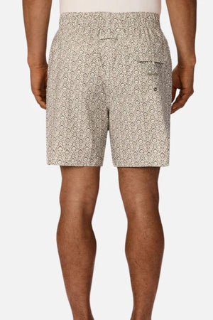 A man is seen from behind wearing Industrie The Montego Swim Short, featuring a beige and white Arabesque pattern, elastic waistband, and back pocket. His arms are relaxed by his sides against a plain white background.