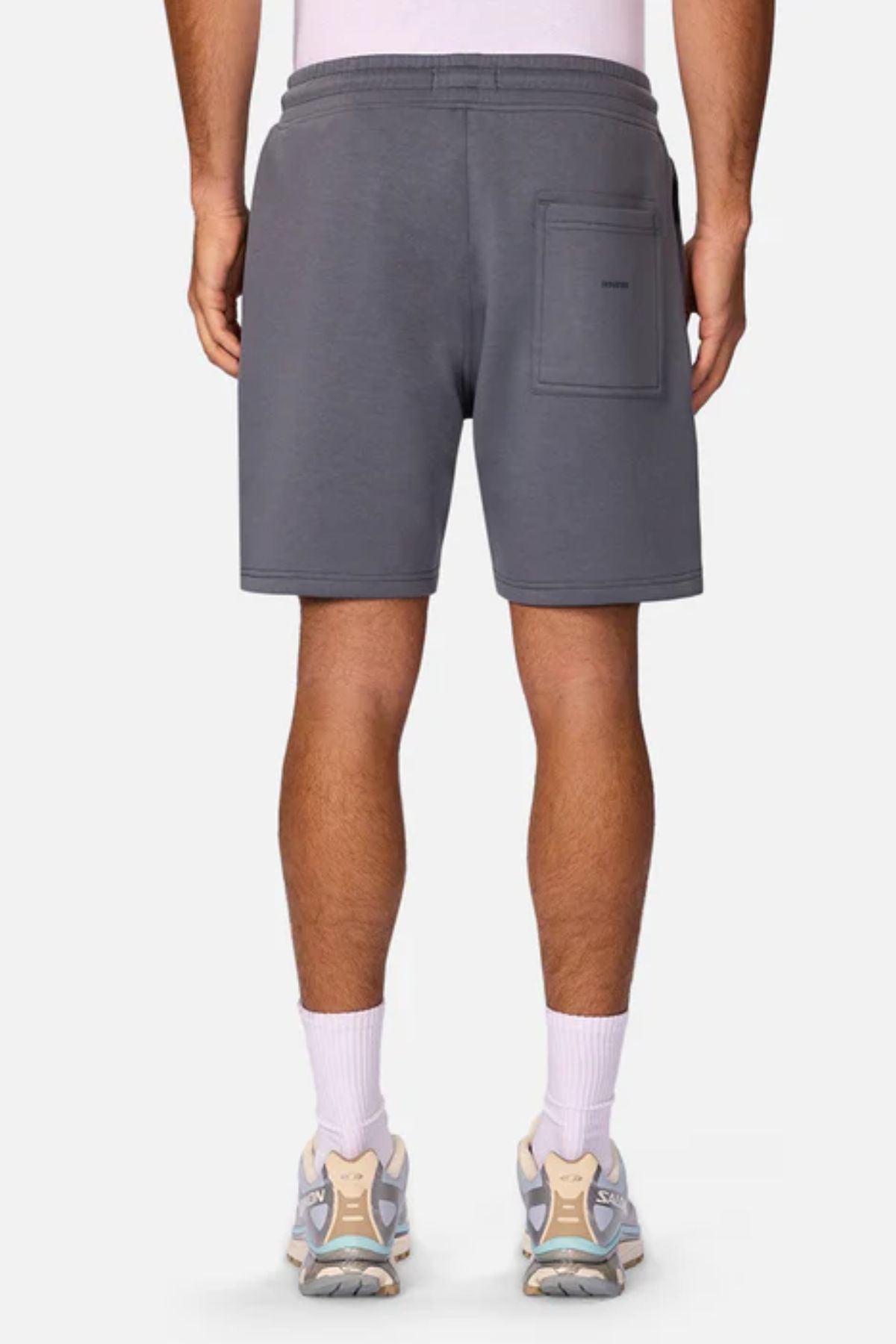 A person is seen from behind wearing Industrie The Tech Track Short in gray, featuring a back pocket, paired with white socks and light sneakers against a plain background.