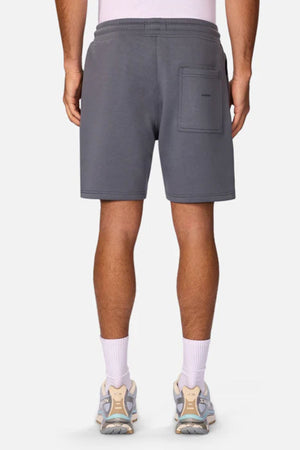 A person is seen from behind wearing Industrie The Tech Track Short in gray, featuring a back pocket, paired with white socks and light sneakers against a plain background.