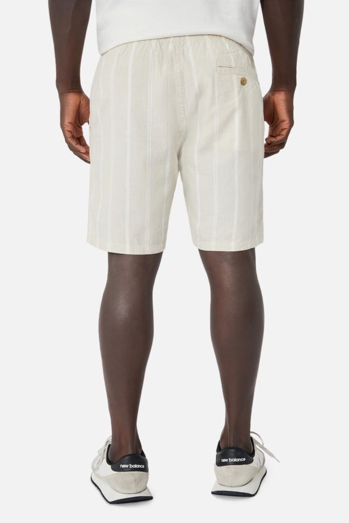 A person effortlessly displays their casual wardrobe in beige and white striped Industrie The Bel Air Shorts, featuring a back pocket button. They pair this with white New Balance sneakers, creating an ensemble that exudes laid-back style against a plain light background.