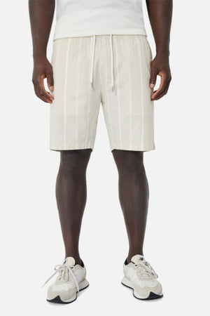 A person wearing a white t-shirt, Industrie The Bel Air Short featuring an elastic waistband, and white sneakers stands against a plain background.