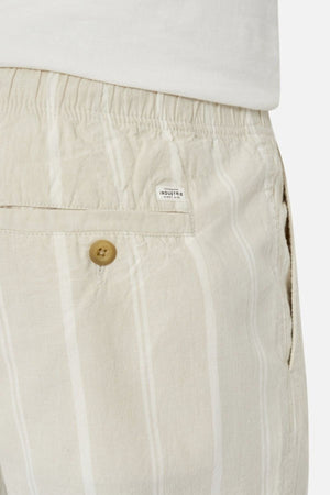 Close-up of a person wearing Industrie The Bel Air Short, showcasing beige and white stripes, an elastic waistband, and a buttoned back pocket. A small label sewn above the pocket adds a stylish touch to this casual wardrobe essential. The person completes the look with a crisp white shirt.
