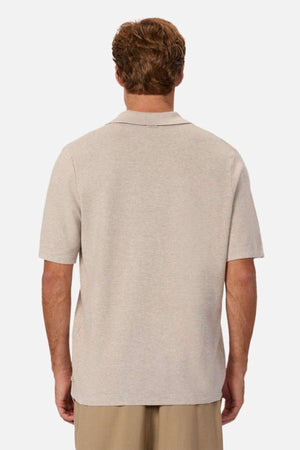 A person with short hair is seen from behind, wearing a light beige Industrie The Hampshire Polo. Embracing a casual style with light brown pants, the individual exemplifies comfort. The Hampshire Polo featured adds a touch of sophistication, standing out against the plain white background.