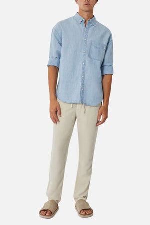 A person wearing Industrie's The McKinley Long Sleeve Shirt in light blue, with sleeves rolled up to the elbows, beige drawstring pants, and light brown sandals. The background is plain white.