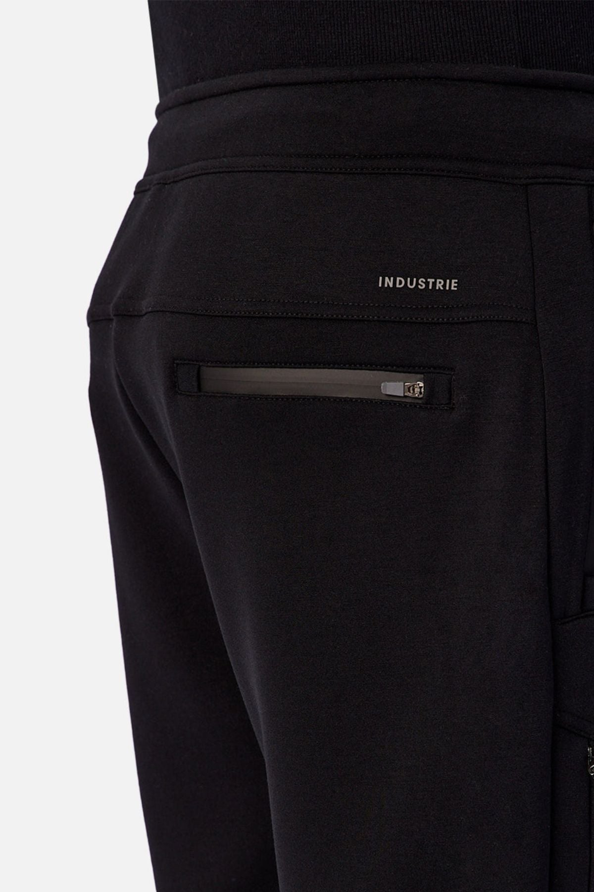 Close-up of the back pocket on Industrie The Tech Armoured Track Pant in black, featuring a zippered pocket and "INDUSTRIE" branding above, highlighting its tactical design.