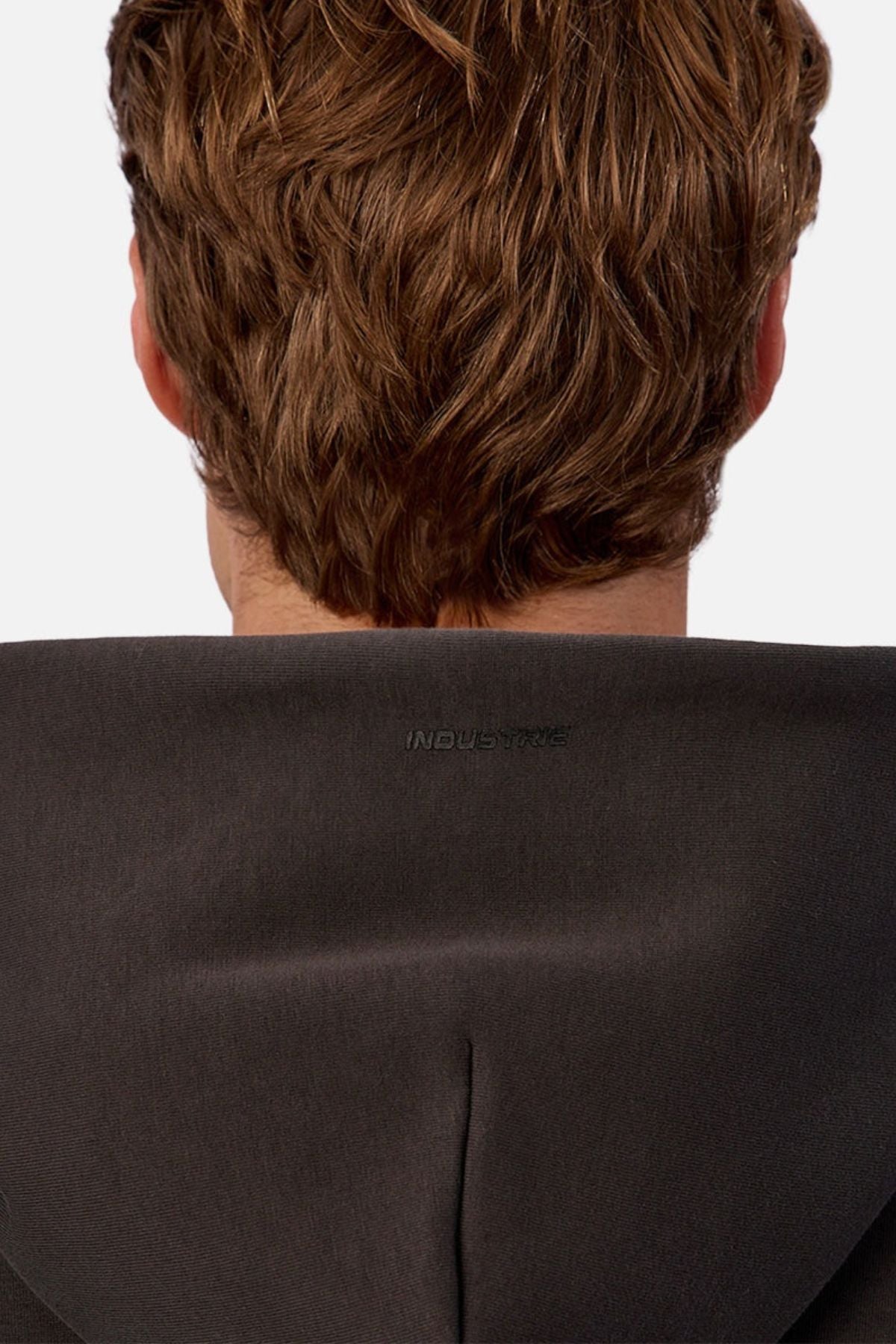 A person with light brown, wavy hair is seen from behind wearing the Industrie The Tech Del Sur Hoodie in a dark color, featuring "INDUSTRIE" printed on the back of the hood.