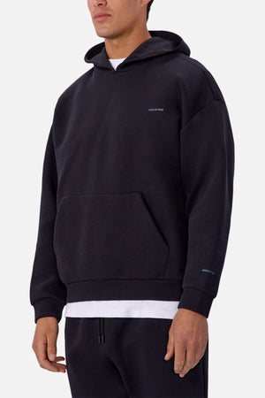 A person wears the Industrie The Tech Del Sur Hoodie in black—relaxed fit, subtle logo, front pocket—layered over a white shirt, standing against a plain light background.