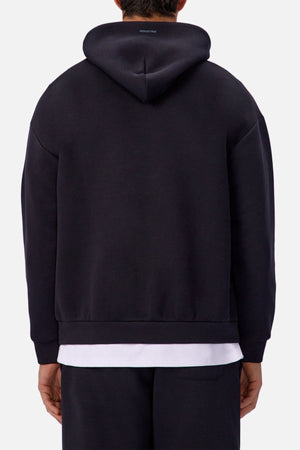 A person is seen from the back wearing the Industrie The Tech Del Sur Hoodie in black over a white shirt and black pants, standing against a plain light background.