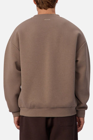A person is seen from the back wearing a loose taupe Industrie The Tech Del Sur Sweat and dark pants against a white background. The athletic sweatshirt features subtle upper-back text, ideal for active lifestyles.