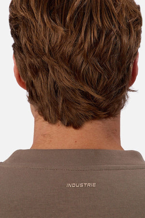 Seen from behind, a person with light brown, wavy hair wears the Industrie The Tech Del Sur Sweat in taupe featuring small white "INDUSTRIE" text near the collar—a stylish sweatshirt ideal for active lifestyles.